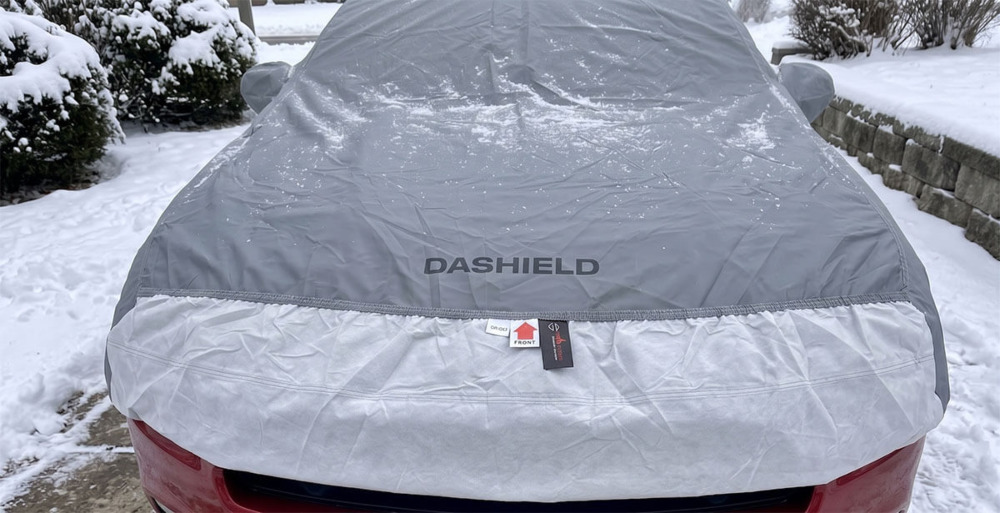 Close-up of the DaShield Ultimum Series cover with its logo and breathable fabric over a red Ford Mustang in NY winter