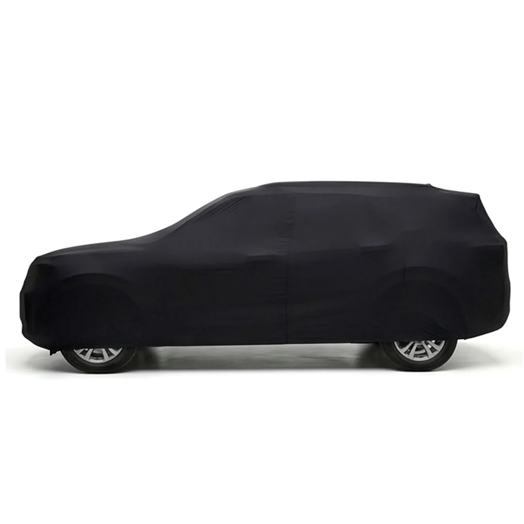 Black car under a satin indoor cover in a home garage with shelving and bicycles nearby