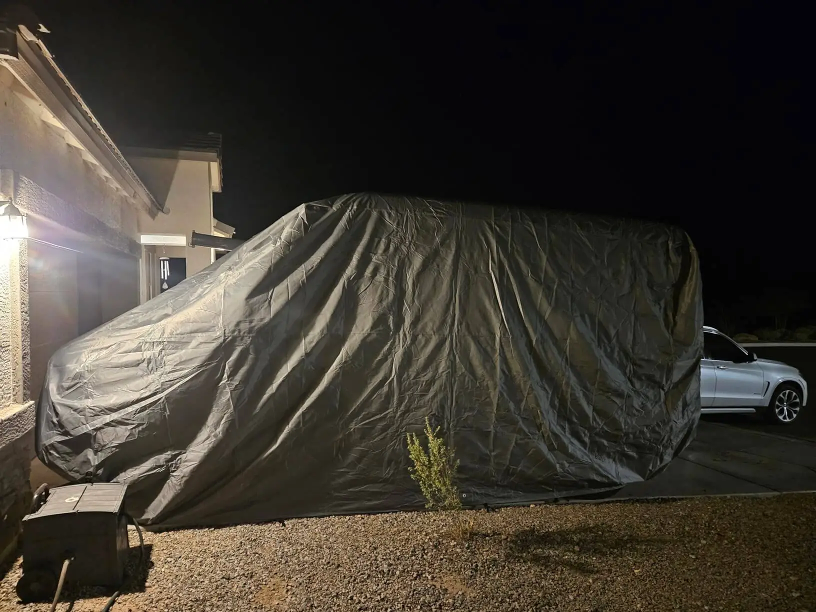 Full-size van under a DaShield Ultimum cover on a gravel driveway at night, hem sitting below the rockers